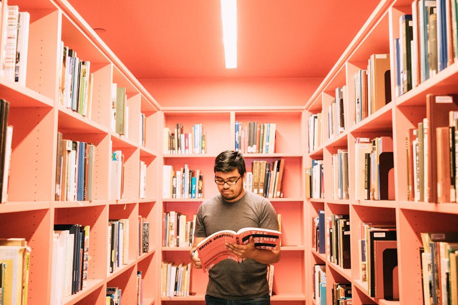 A student reads a book while standing among the stacks of books in the New School library.