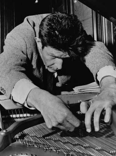Artist John Cage plucks the strings of a piano in the 1950s