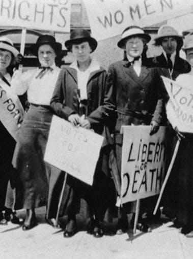 Suffragist women stand in a group with signs in the 1910s