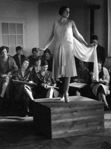 A model in a white dress poses before drawing students in the 1920s