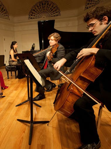 A piano player, violinist, and cellist perform together in Mannes College of Music perform together on a stage