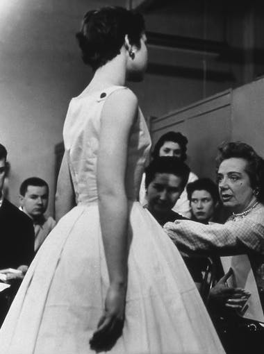 A model in a dress stands in front of fashion students in the 1950s