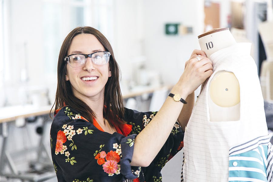 A student in glasses works on a garment on a dressmaker's dummy