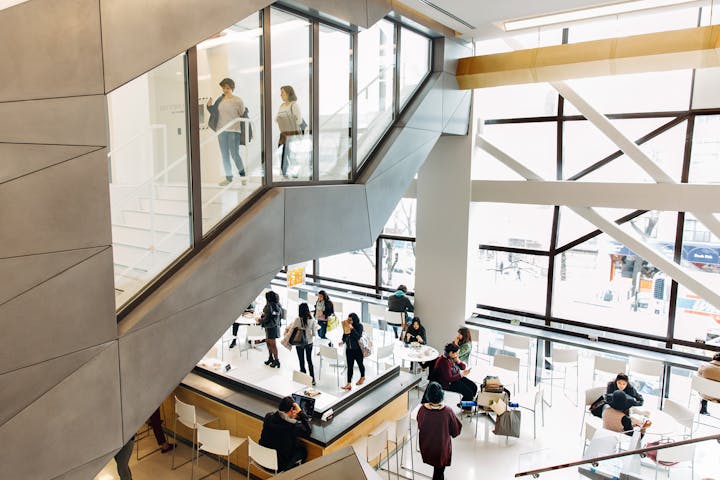 Students climb a staircase over a light-filled cafeteria with large glass windows.