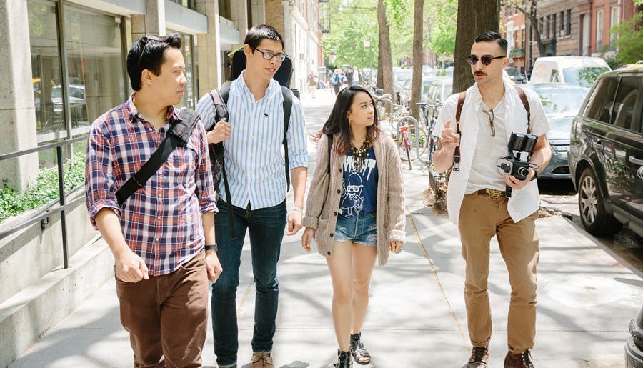 Four students have a conversation while walking down the sidewalk.