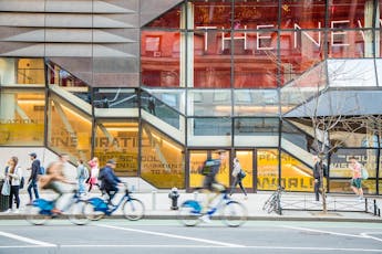 Students on bikes and on foot pass in front of the colorful red and yellow windows of The New School University Center.