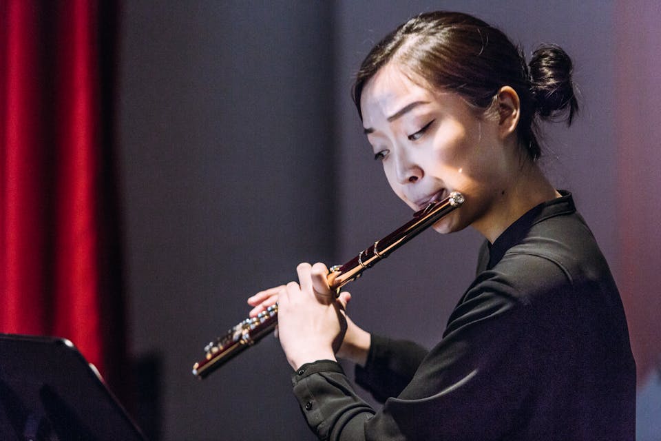 Student dressed in black plays a flute on stage.
