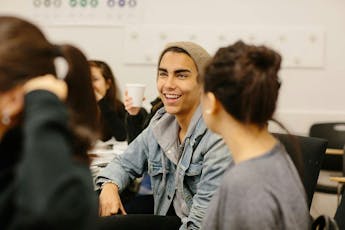 A student smiles while talking to another student in a classroom.